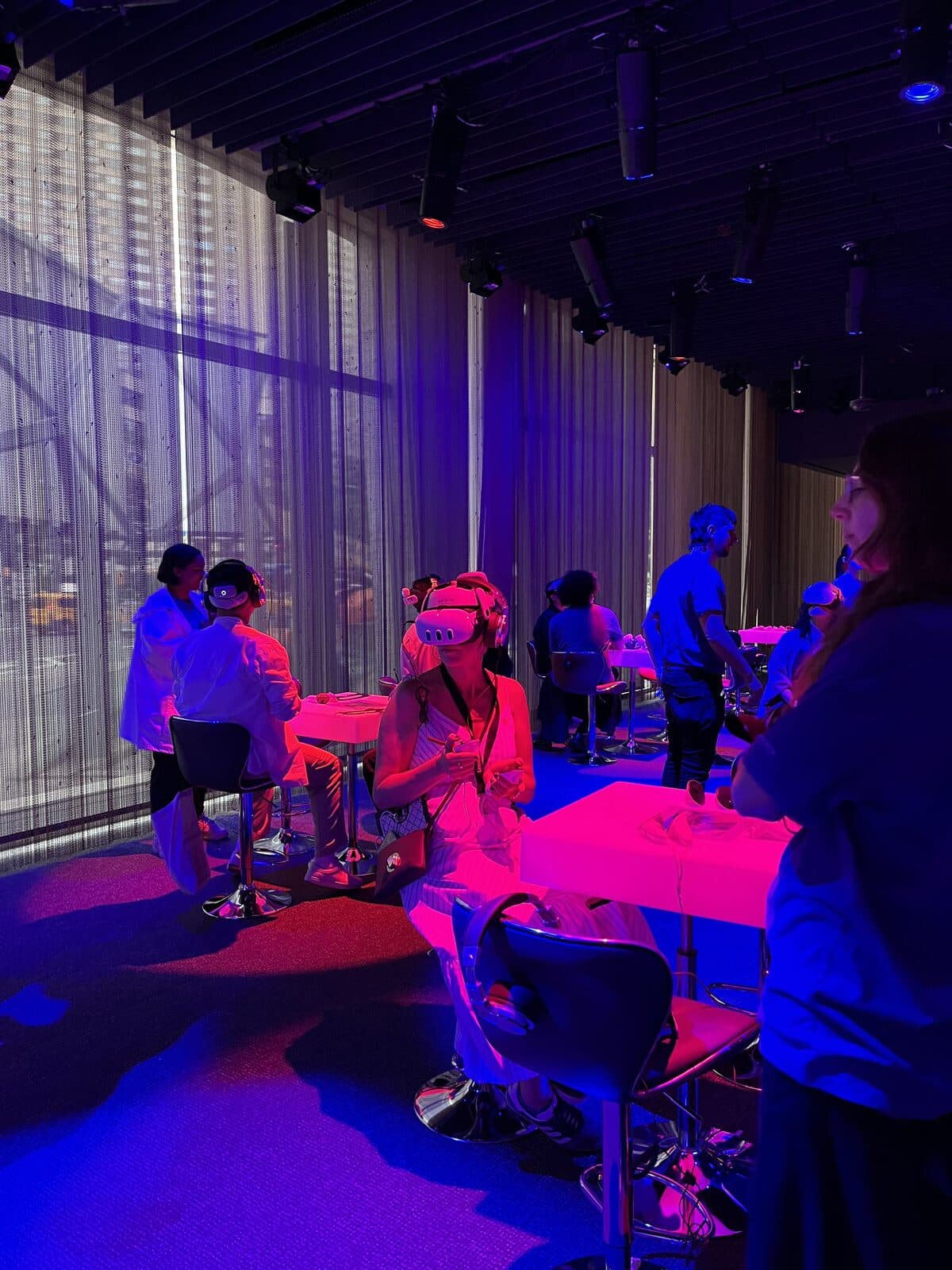 Visitors seated at illuminated tables wearing VR headsets