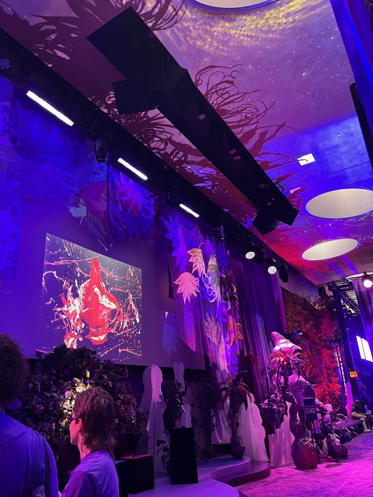 Purple-lit stage with a red paint-splash projection and greenery installation